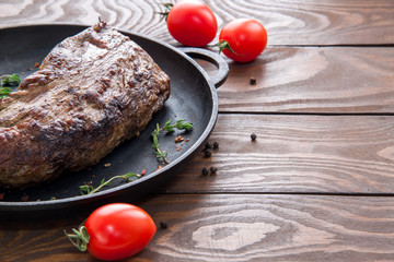 roast beef steak sprinkled with herbs and spices on a black iron frying pan on a wooden table with cherry tomatoes and space for text on the right