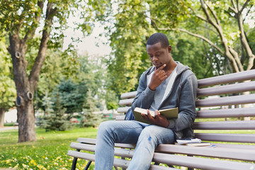 Fototapeta premium Young man reading book in park copy space