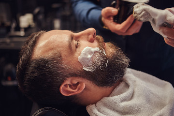 Master hairdresser prepares the face for shaving and smears the face with foam in a hairdressing salon.