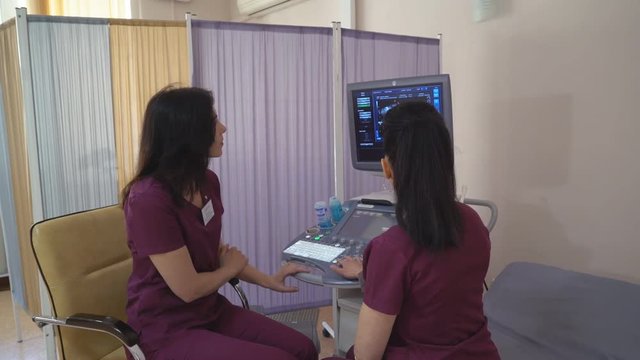 medical center for family planning. two attractive women doctors gynecologists sitting in the ward and looking at the four dimensional ultrasound scan of baby. on the screen of a 2D 3D 3D image of a