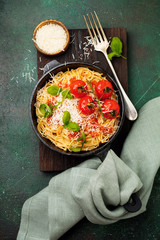 Traditional Italian dish of spaghetti with tomato sauce and parmesan cheese in iron frying pan on dark old concrete background. Selective focus. Top view.