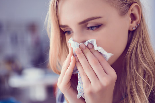 Girl blows her nose into a tissue. Portrait of a woman with tissue in hands looking away. Concept of treatment for allergies or the common cold.