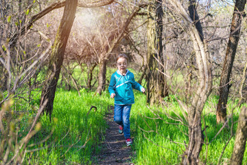 Naklejka na ściany i meble Little girl runing along the forest path, a bright photo of spring.