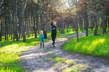 Fototapeta premium Morning jogging, mom and daughter are running along the forest trail, free space.