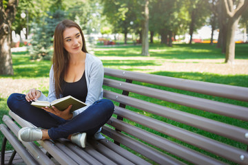 Obraz premium Young asian woman sitting on a bench in the park. Relaxing and reading a book