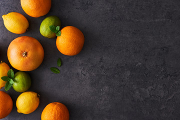 Top view of fresh ripe citruses. Lemons, limes, oranges and grapefruits on dark concrete background. Flat lay with copy space on the right.