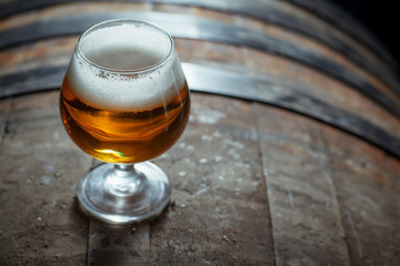 Snifter beer glass on a wooden barrel