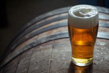 Glass of light beer on a wooden barrel