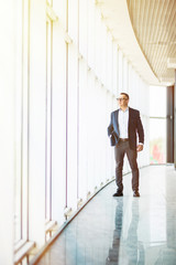 full length picture of a mid aged business man walking towards the camera and smiling in office building