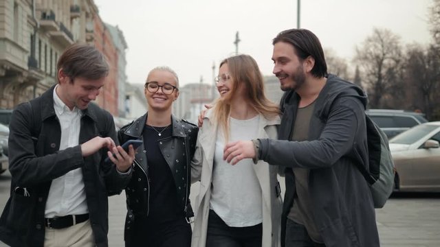 Group of four friends laughing out loud outdoor, sharing good and positive mood, happy friends students on street park, university campus, phone smiling people