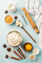 Baking background with ingredients flour, eggs, sugar, butter, cinnamon, anise star and kitchen tools on blue rustic table. Selective focus. Top view.