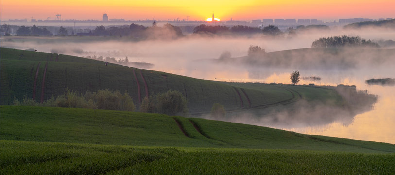 Misty Sunrise Over A Lake Surrounded By Green Hills