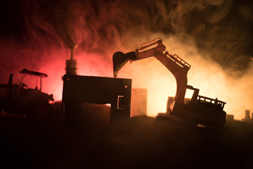 Construction site on a city street. A yellow digger excavator parked during the night on a construction site. Industrial concept table decoration on dark foggy toned background