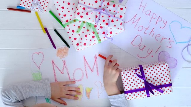 Little girl drawing happy mother's day greeting card with presents on the table.
