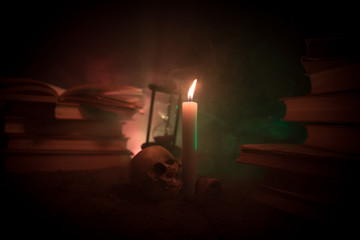 Wizard's Desk. A desk lit by candle light. A human skull, old books on sand surface. Halloween still-life background with a different elements on dark toned foggy background.
