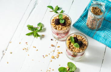 Healthy layered dessert with yogurt, granola, jam, blackberry in glass on wood background