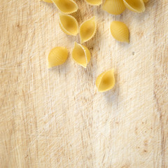 Dry shell macaroni on rustic wooden surface close up, conchiglie pasta, basic food of delicious Mediterranean meals