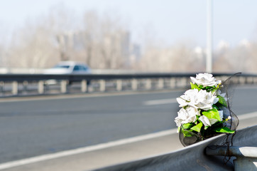 Artificial white roses flowers on the site of a car crash traffic accident on the bridge safety metal fence with a fatal outcome with vehicle movement