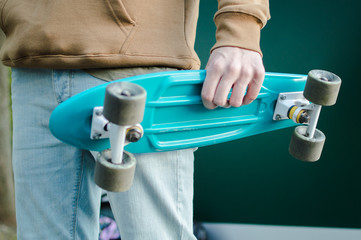 Blue pastic penny skateboard in the hand of the young modern man weared in brown hoodie and blue jeans. Concept of the modern transport solutions, commute.