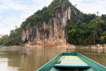 Boat on the Mekong River in front of a limestone cliff where the famous Pak Ou Caves are set. They are located near Luang Prabang in Laos.