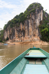 Boat on the Mekong River in front of a limestone cliff where the famous Pak Ou Caves are set. They are located near Luang Prabang in Laos.