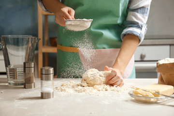 Woman sprinkling flour over dough on table in kitchen