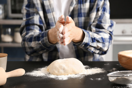 Man sprinkling flour over dough on table in kitchen