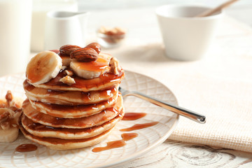 Stack of tasty pancakes with banana, nuts and syrup on table © New Africa