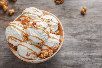 Tasty ice cream with caramel sauce and popcorn in bowl on wooden table, top view