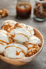 Tasty ice cream with caramel sauce and popcorn in bowl on wooden table