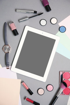 Flat lay composition with tablet and makeup products for woman on grey background