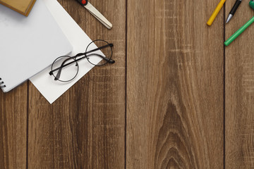 A blank sheet of paper, a notebook, pens, glasses, scissors on a wooden table top, space for text