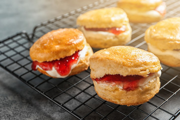 Tasty scones with clotted cream and jam on cooling rack, closeup