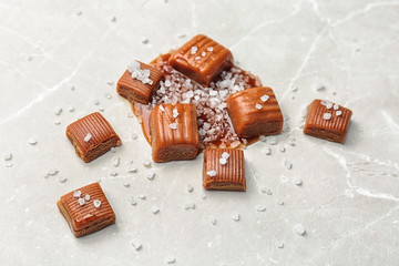 Delicious candies with salted caramel sauce on light background