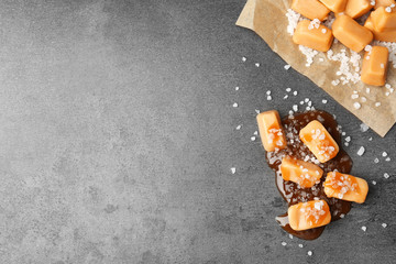 Delicious candies with caramel sauce and salt on gray background