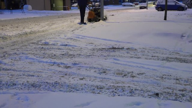 Sweeper man removing snow with snowblower after snowstorm at night. 4K