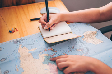 Close-up of women hands pointing at on world map on table. And one hand holding a pen to write on...