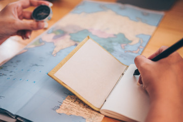 Close-up of women hands pointing at on world map on table. And one hand holding a pen to write on notebook and using finger pointing on world map.