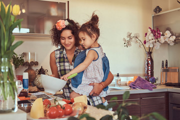Beautiful Hispanic mother teaches her cute little daughter prepare pizza in the kitchen.