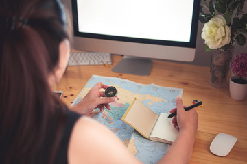 Happy woman planning vacations on line searching information in map and laptop at home office. Holding compass and writing on notebook