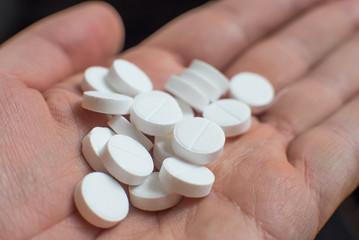 White pills in hand on black background closeup