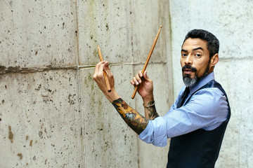 Portrait of a tattooed man drumming on a concrete wall