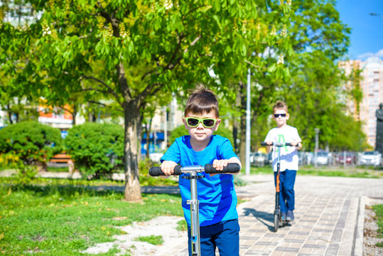 Two little kids boys riding on push scooters.
