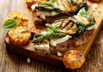 Vegetarian sandwich. Wholemeal bread sandwiches with feta cheese, grilled zucchini, green asparagus, sugar peas, olive oil and herbs on a wooden table. Healthy and delicious food