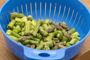 Grüner Spargel geschnitten in Stücke in einem blauen Küchensieb