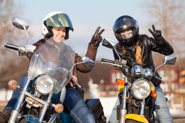 Fototapeta na wymiar Victory signs in leather gloves from two laughing female bikers with street motorcycles