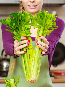 Woman in kitchen holds green celery