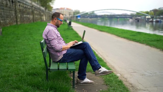 Young man sitting with laptop on bench in the park 
