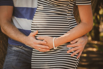 Close up portrait of happy pregnant woman together with husband hugging in summer park