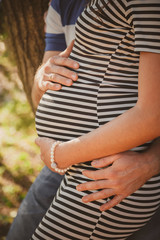 Close up portrait of happy pregnant woman together with husband hugging in summer park